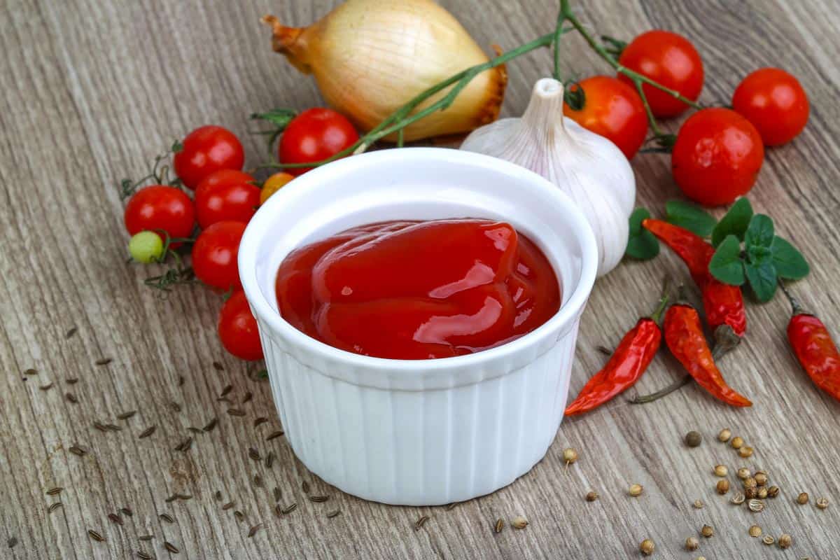 A cup of tomato ketchup on a wooden table.